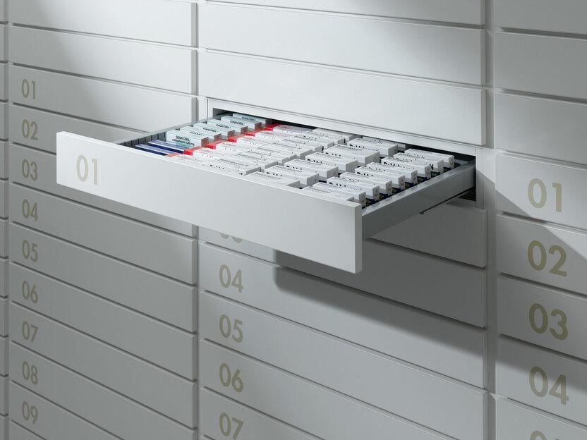 Detailaufnahme von schmalen weißen Medikamentenschubläden mit dezenter Nummerierung und sichtbarer Medikamentenaufteilungen.