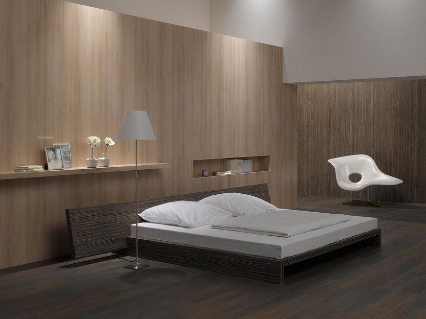 Schlafzimmerimpression von Bett, Nachtisch und Sideboard mit Holzverkleidung an Wand und indirektert Beleuchtung