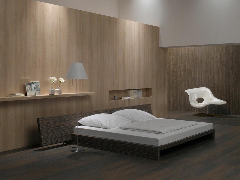 Schlafzimmerimpression von Bett, Nachtisch und Sideboard mit Holzverkleidung an Wand und indirektert Beleuchtung