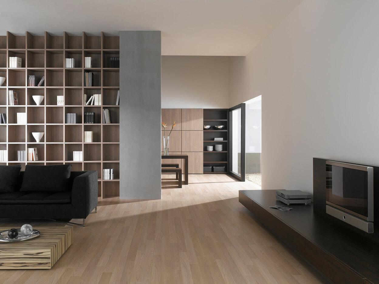 Offene Wohnraumimpression mit Einbauregal für Bücher und Dekoration in Trennwand mit hellem Holzboden
